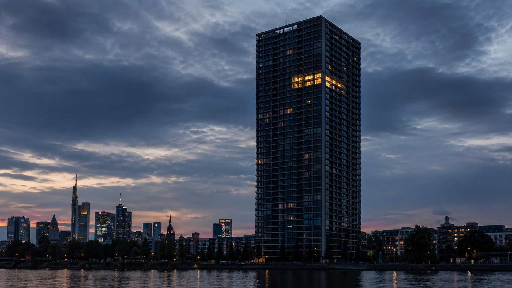 Tall residential tower in Frankfurt at dusk, a single apartment lit on the upper floors
