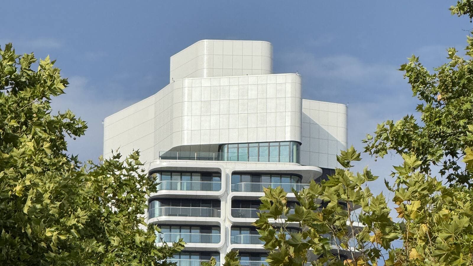 The crown of Grand Tower Frankfurt showing the penthouse setback above the topmost residential floors, framed by trees