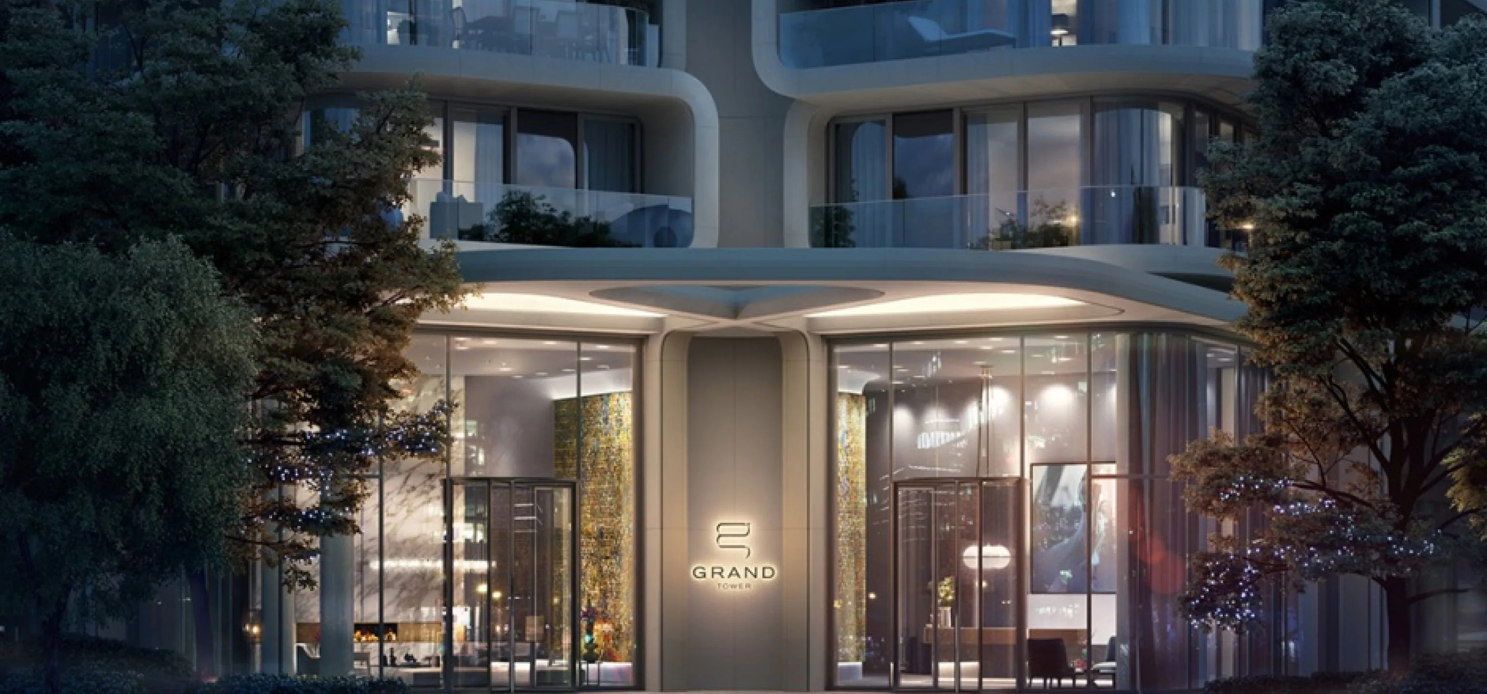 Grand Tower entrance at dusk — illuminated lobby behind glass, framed by trees