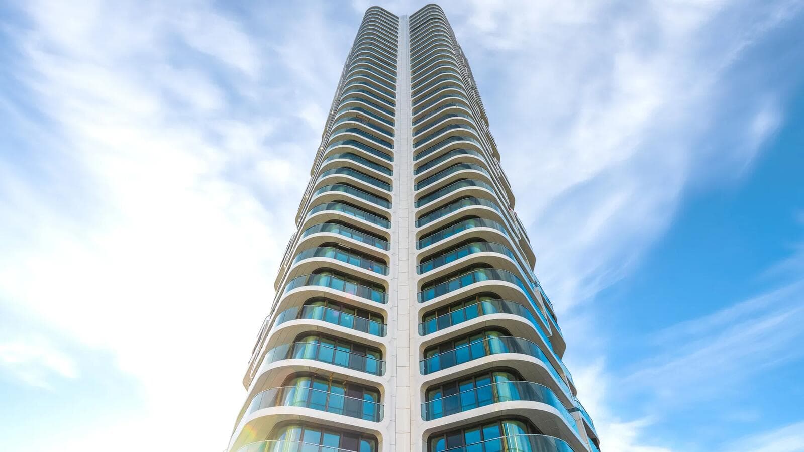 Grand Tower photographed from the base looking up, the balcony bands stacking floor by floor to the twin crown against a blue sky